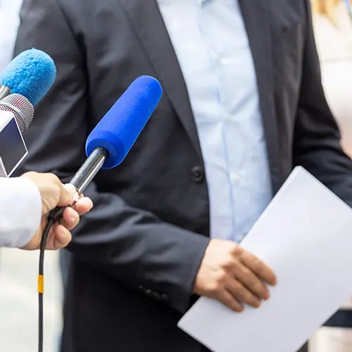 Businessperson holding documents, speaking to multiple microphones