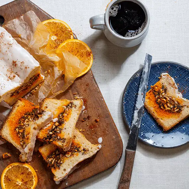 Cake on a cutting board garnished with orange peels and a dark beverage on the side