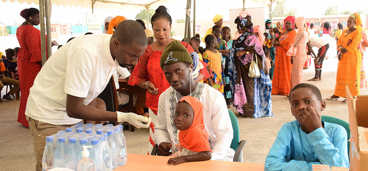 Male nurse checking blood pressure of woman sitting in front of olam banner whilst holding baby