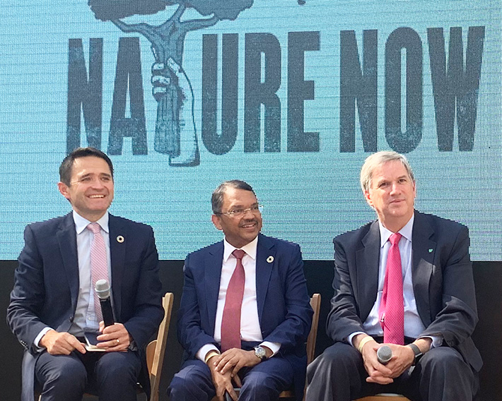 Three men on sitting on a stage in front of a mural that has the words nature now