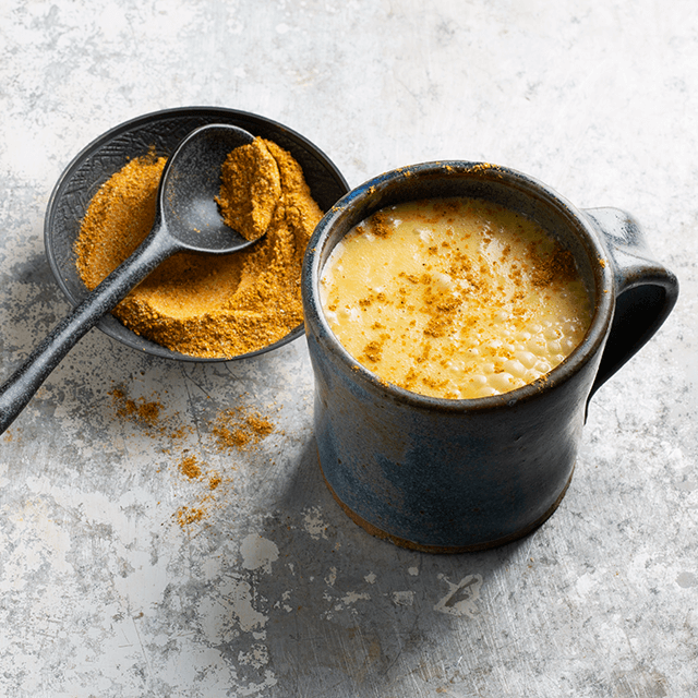 Bright yellow chai latter in a black mug with a bowl filled with curcuma spices