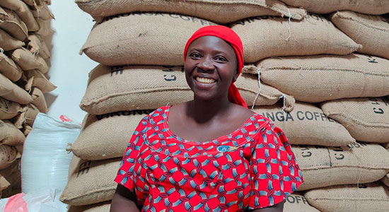 Female farmer smiling and posing in front of a bunch of burlap bags stacked on top of each other