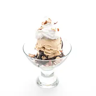Ice cream dessert that is topped with whipping cream, chocolate sauce and a sprinkle of nuts