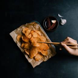 A person eating a plate of chips with chopsticks