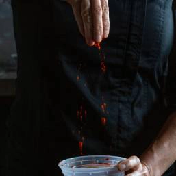 A chef sprinkling seasoning into a bowl