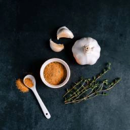Spice mix, garlic, two garlic cloves, and a few branches of thyme spread on a black surface