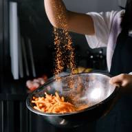 A chef sprinkling seasoning over a bowl of potatoes