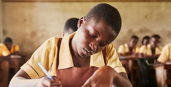 Close up shot of a girl sitting behind a school desk doing school work