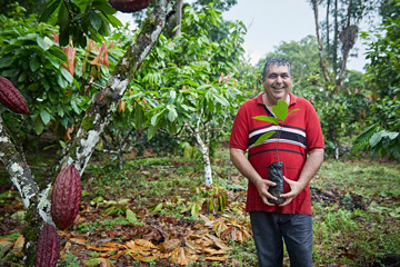 Brazilian man wearing a red shirt posing with a plant with a forest in the background