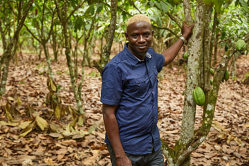Man from Côte d’Ivoire standing in a cocoa plantation posing for the camera