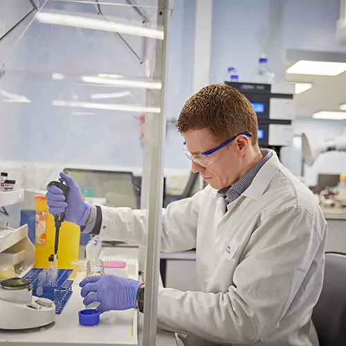 Male lab technician in lab clothing inserting samples in a tube