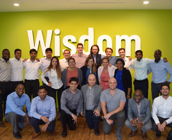 Group photo of the future leader team standing infront of a wall that has the words wisdom written on it