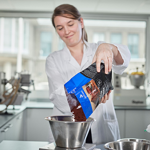 Woman smiling and pouring cocoa powder into a metal bowl