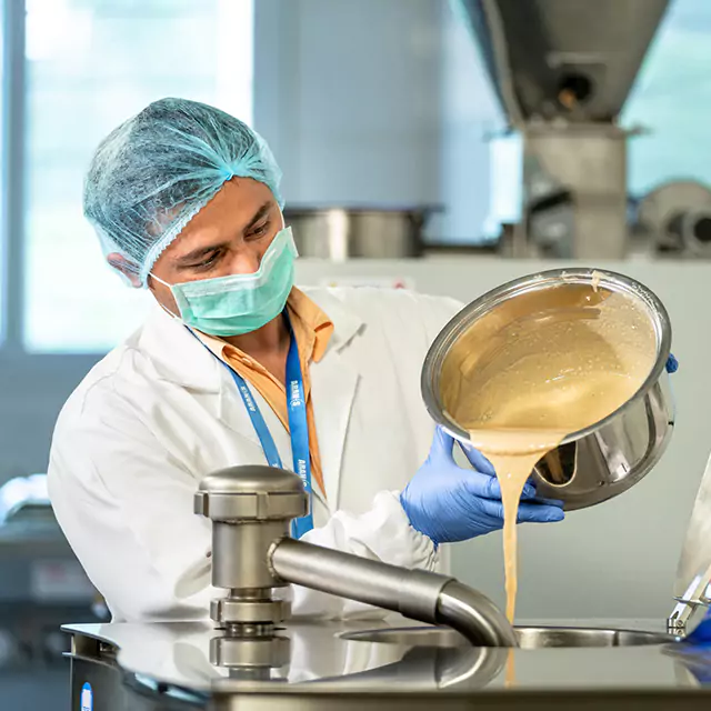 Male factory worker in protective gear pouring liquid into industrial mixer