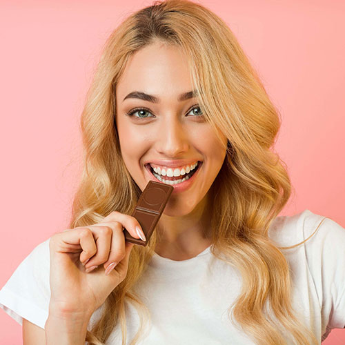 Close up shot of a woman with blonde hair smiling and eating a piece of chocolate