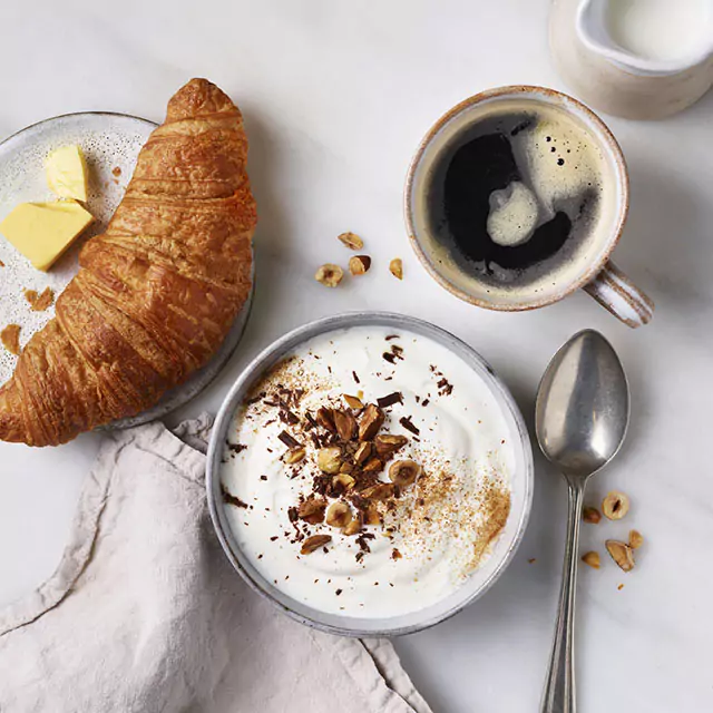 Above shot of a croissant, yogurt with nuts, coffee, and milk on the side