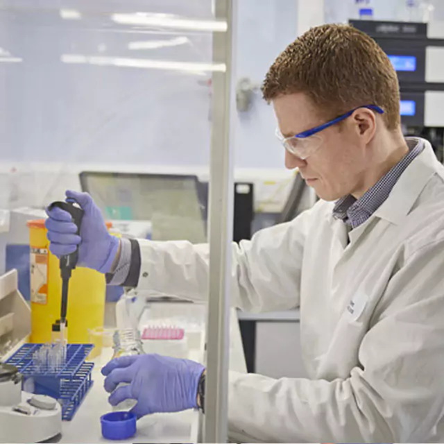 Britannia logo. Employee pouring liquid into a glass and handling samples in a tube