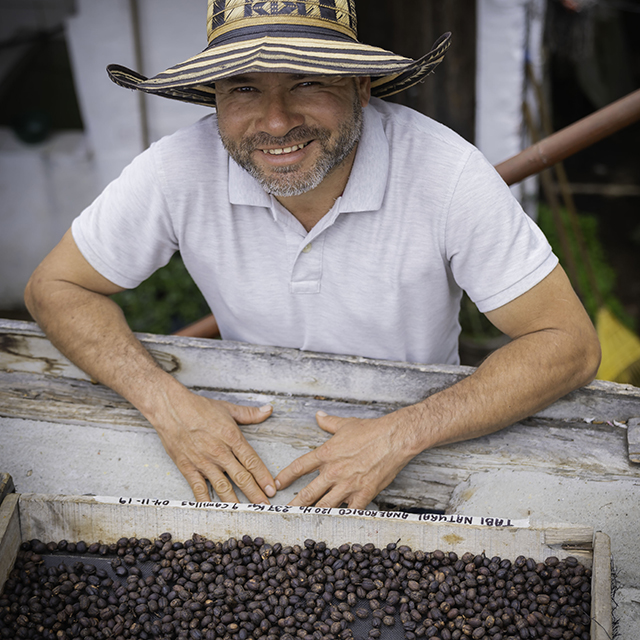 Colombian farm worker posing in front of roasted coffee beans