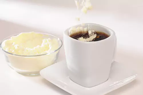 Close up shot of coffee with powdered milk and a small bowl of milk powder on the side