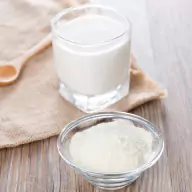 A glass of milk with a side cup of milk powder
