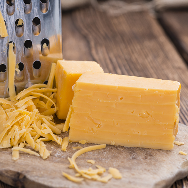 Close up shot of a block of cheddar cheese with grated cheese on the side