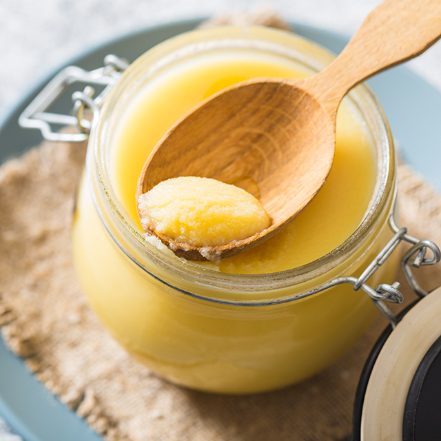 Close up shot of ghee in a mason jar and a scoop of ghee on a wooden spoon