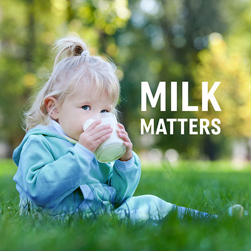 Toddler sitting on a grass field while drinking milk the words milk matters