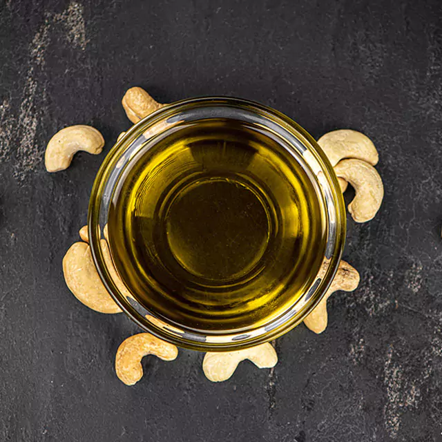 Close up shot of nut oil with cashew nuts scattered around the oil