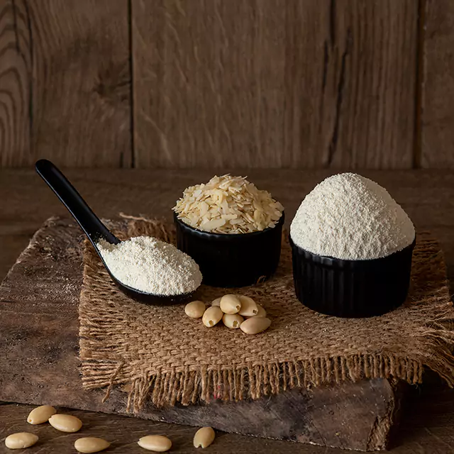 Styled medium shot of nut flour with peeled almonds scattered around