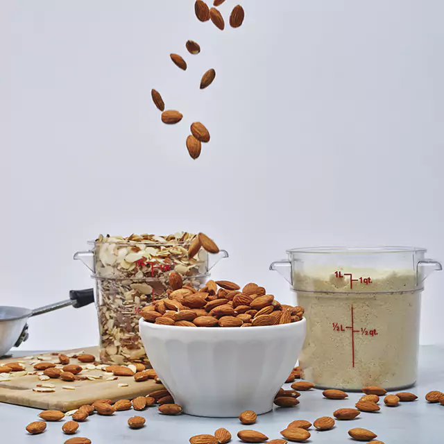 Bowl of almonds with measuring cups of crushed almonds and almond flour