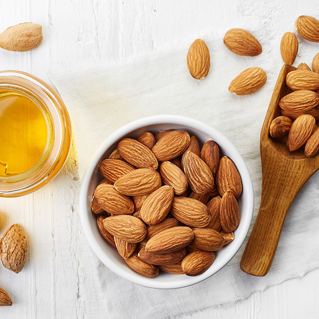 Close up shot of almonds in a white bowl and a small glass bottle filled with almond oil