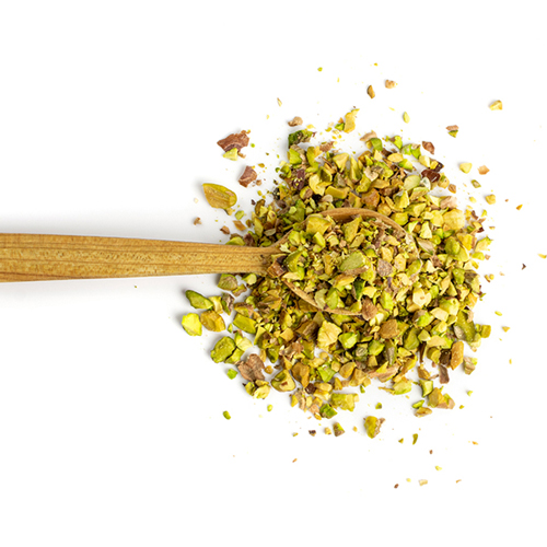 Closed up shot of crushed pistachios sprinkled around a wood spoon