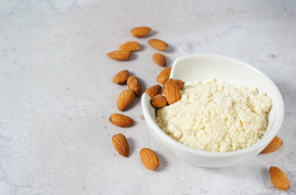 Close up shot of nut based protein power in white bowl with scattered almonds 