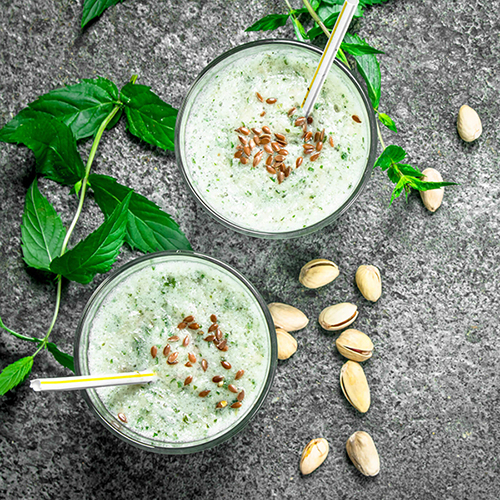 Above shot a green smoothie decorated with shelled pistachios and a green mint leave