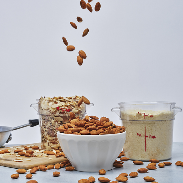 Medium shot of a bowl filled with almonds and two measuring cups with crushed almonds and almond flour.