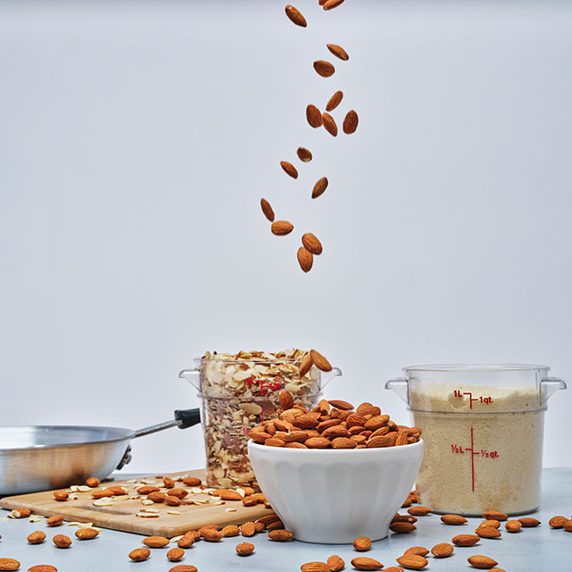 Medium shot of a bowl filled with almonds and two measuring cups with crushed almonds and almond flour