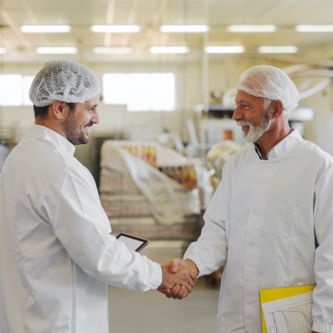 Two men wearing overall and a hair nets shaking hands