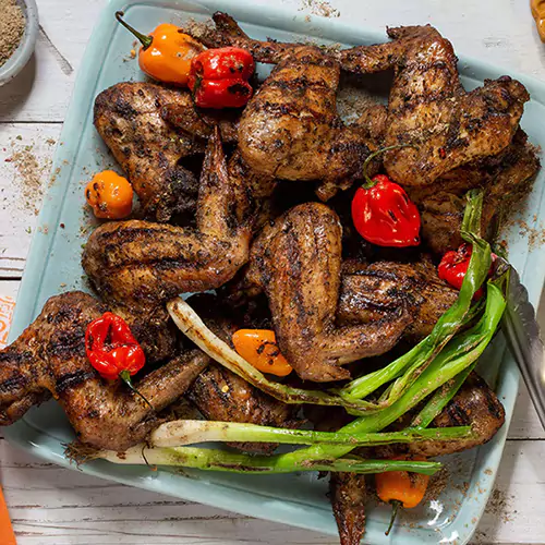 Close up shot of Caribbean chicken wings decorated with chilies and roasted spring onions