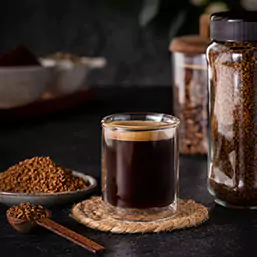 A cup of dark cofee with a bowl and a spoon of freeze dried soluble coffee