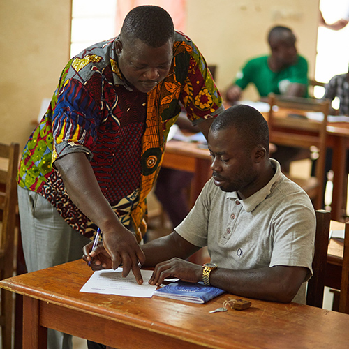 Male teacher showing one of his seated students something on a page